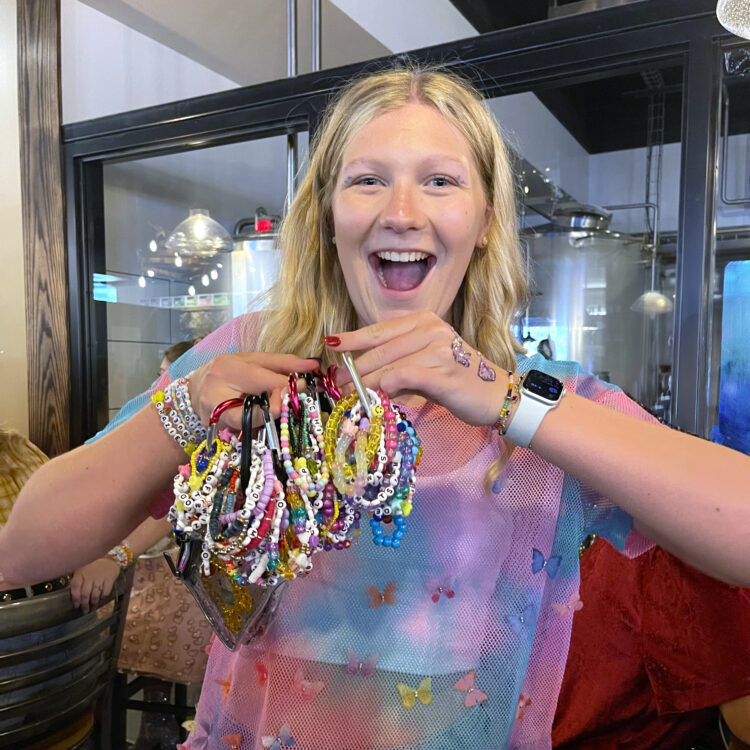 smiling blonde girl holding up many beaded bracelets on carabiner clips