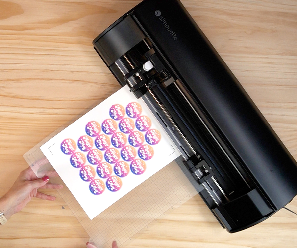 Loading sticker sheet on cutting mat into a black Silhouette Cameo 5 cutting machine