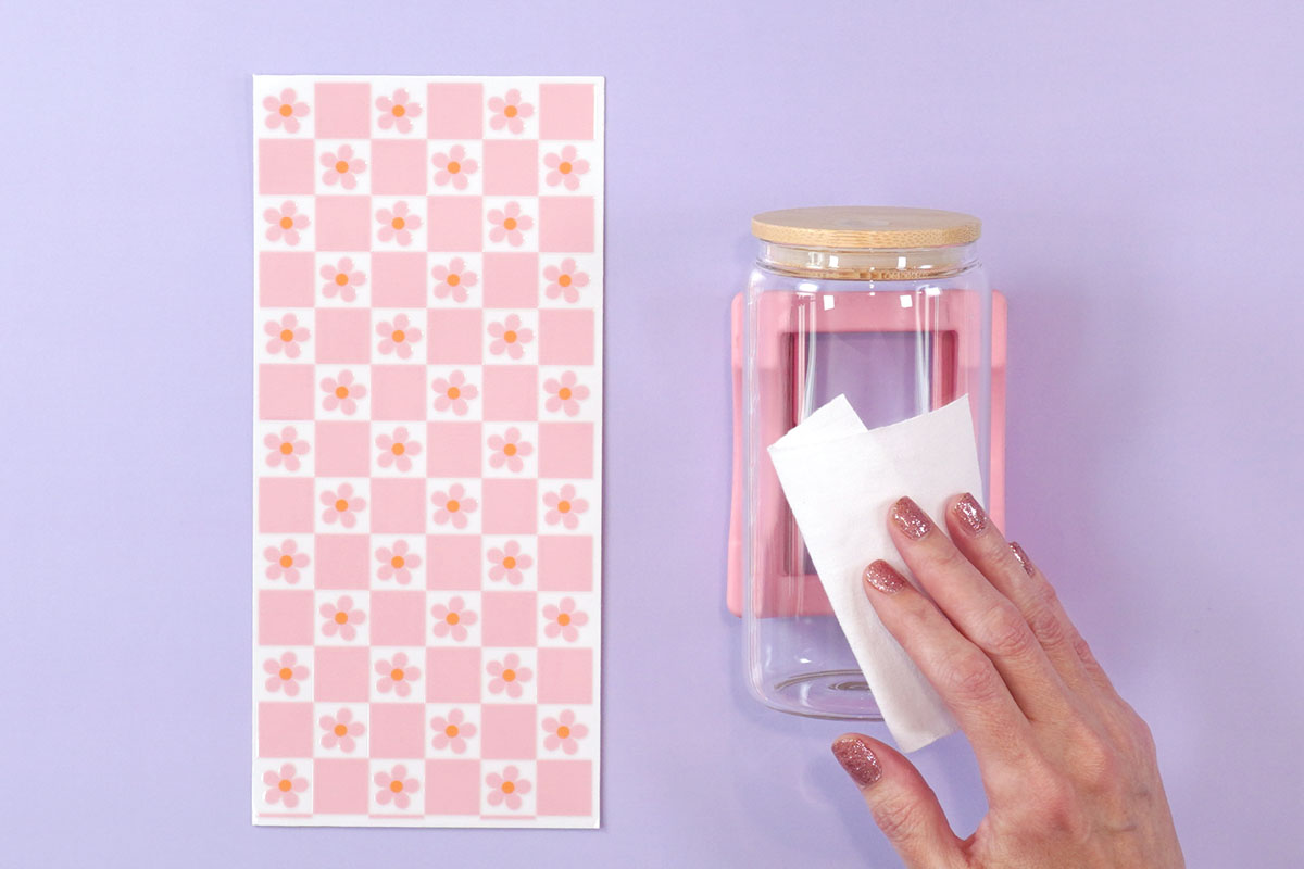 Hands cleaning a glass cup with a white lint-free cloth on lavender background