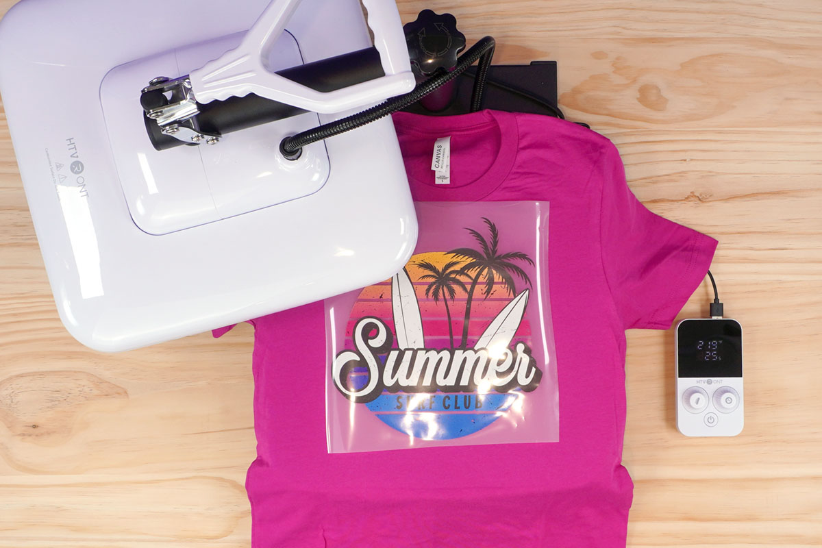 Overhead view of hot pink shirt with unpressed "Summer Surf Club" DTF transfer on the open HTVRONT Manual Heat Press Machine