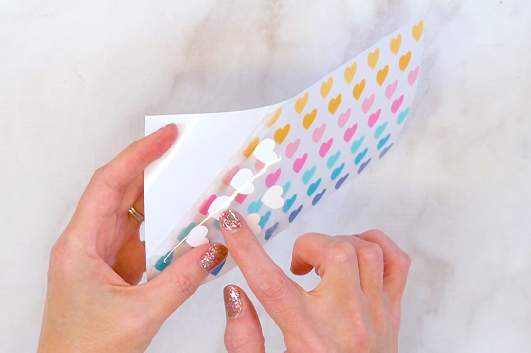 Close-up of hands peeling back a UV DTF cup wrap to show the different layer components