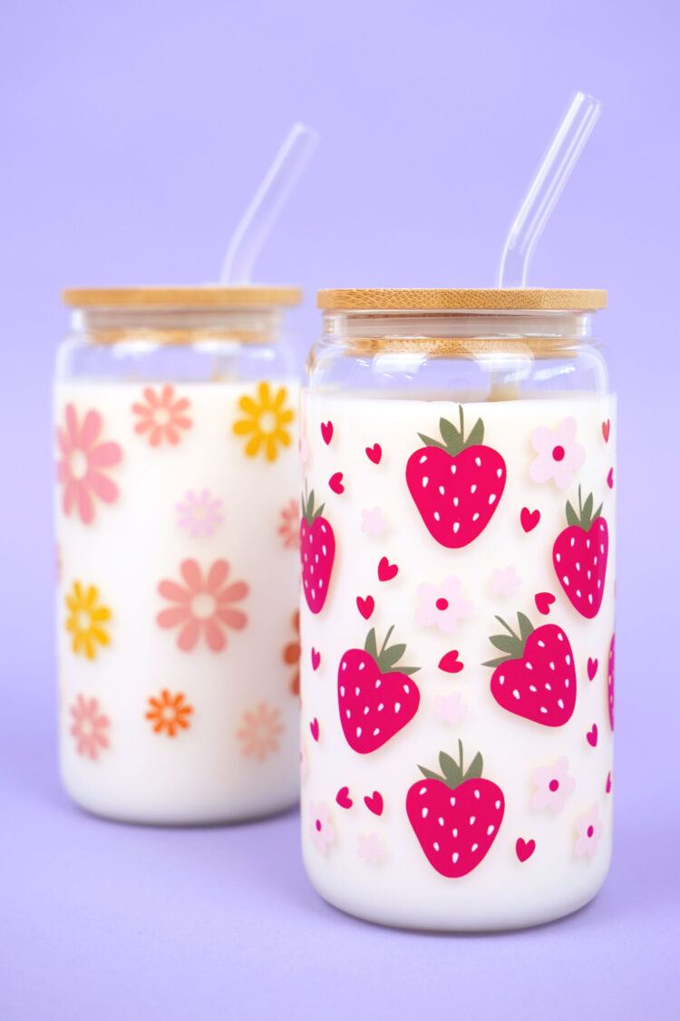 Two glass can cups with UV DTF patterned tumbler wraps with flowers and strawberries on light purple background