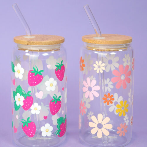 Two glass can cups with UV DTF patterned tumbler wraps with flowers and strawberries on light purple background