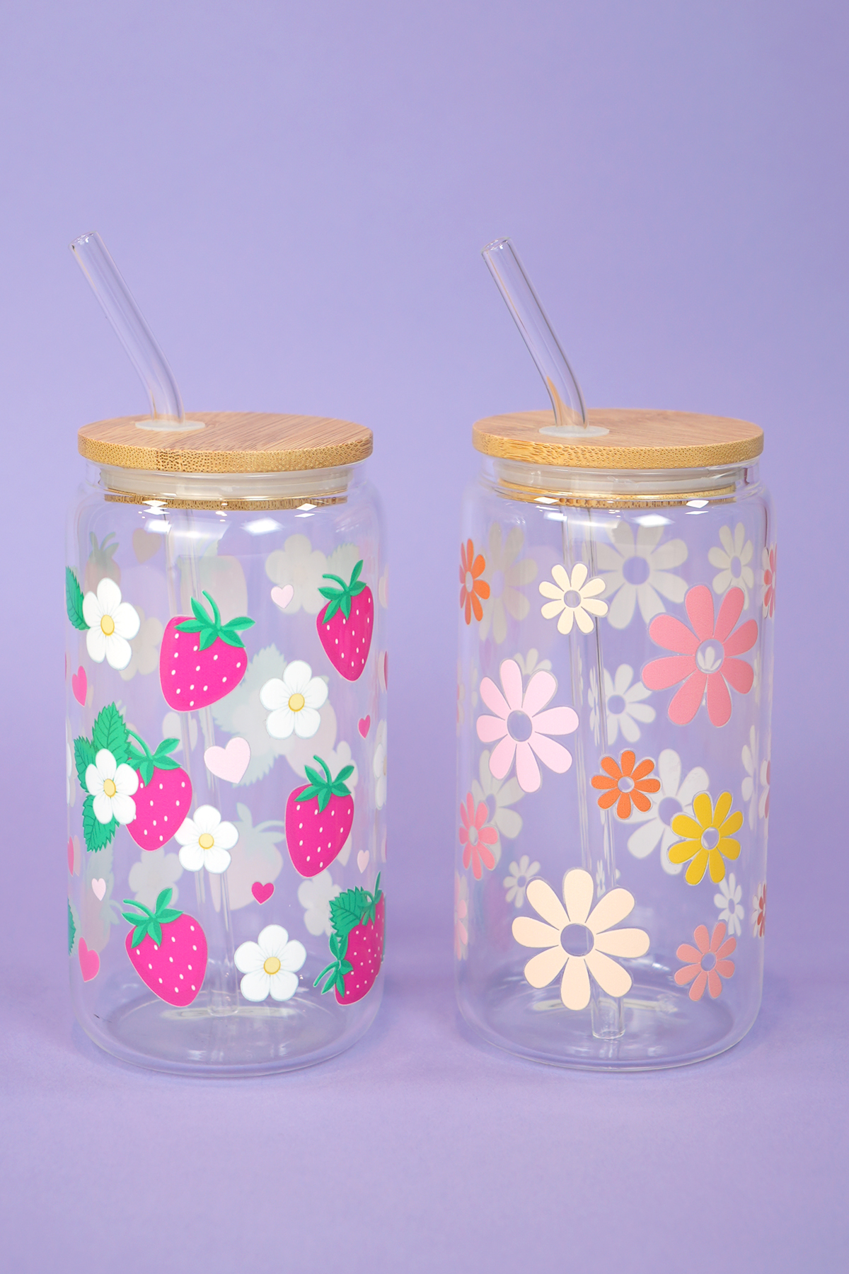 Two glass can cups with UV DTF patterned tumbler wraps with flowers and strawberries on light purple background