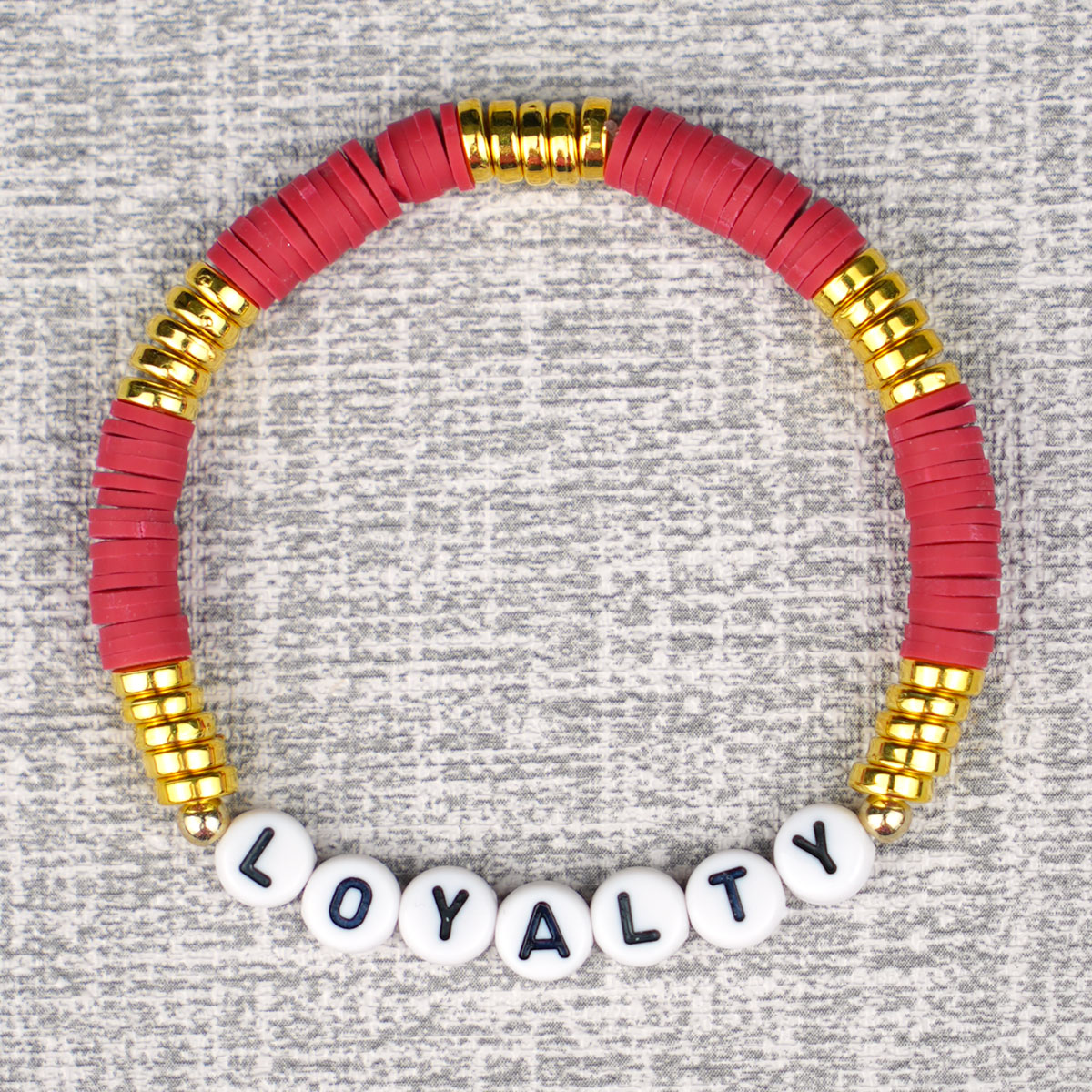 red and gold beaded bracelet with "Loyalty" alphabet beads on grey background