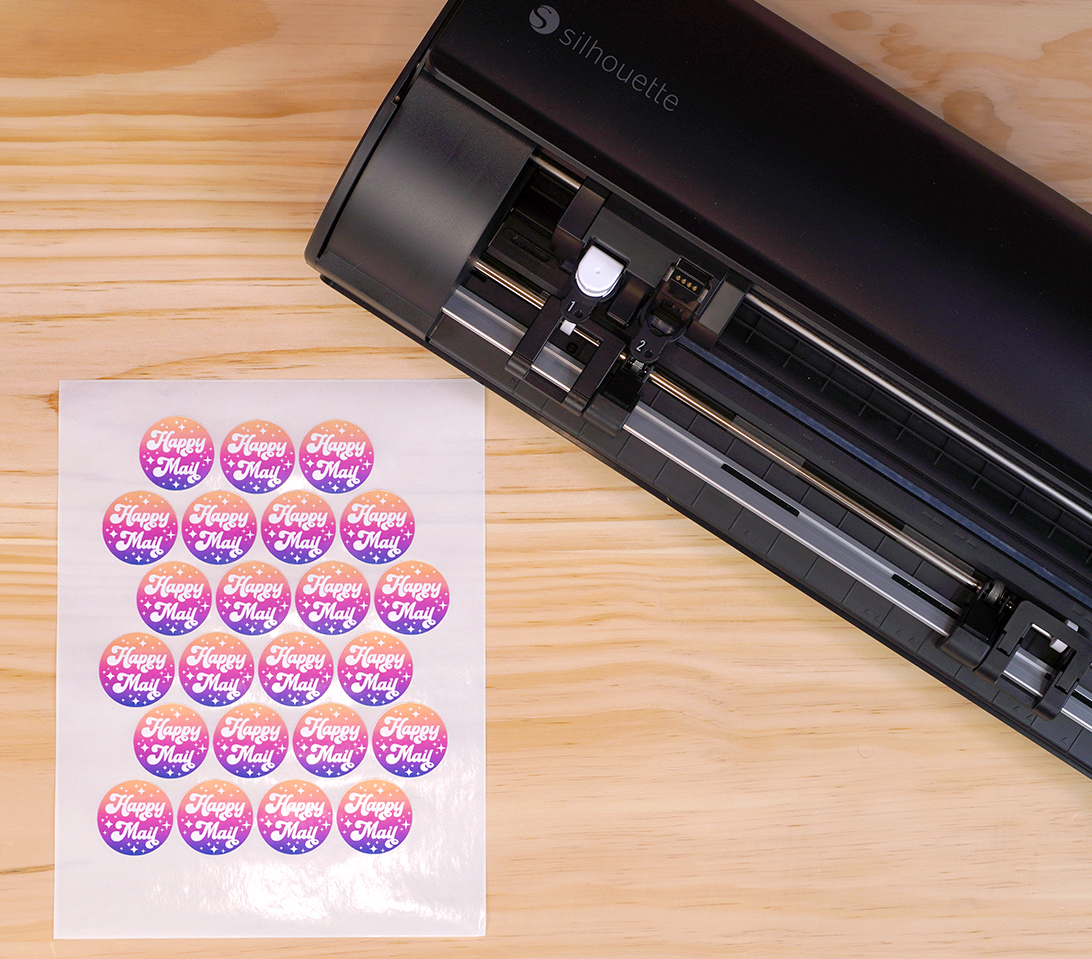 Sheet of kiss-cut stickers on a wood table next to black Silhouette Cameo 5